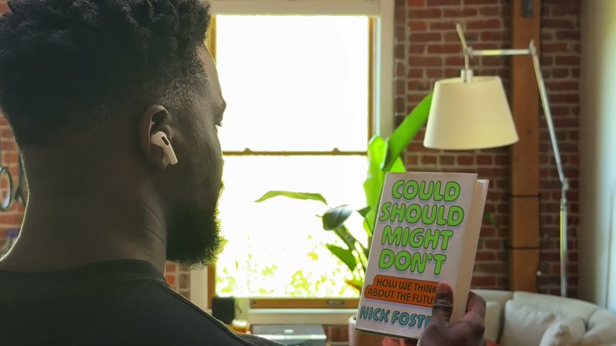 A person wearing AirPods holds up the book Could Should Might Don’t in Apple’s Visual Intelligence demo