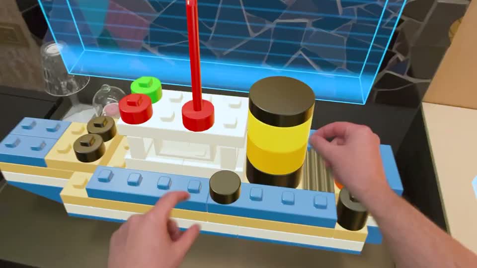 Two hands reaching toward a blue, white, and yellow virtual block boat in Blockworks on Apple Vision Pro