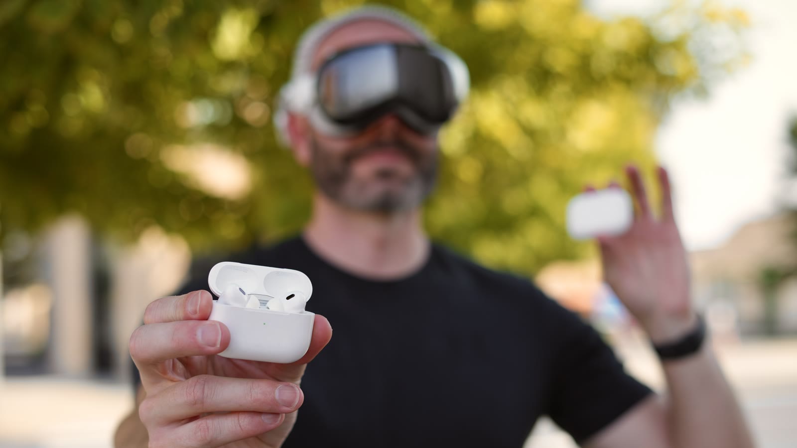 Justin Ryan wears Apple Vision Pro while holding an open AirPods case toward the camera
