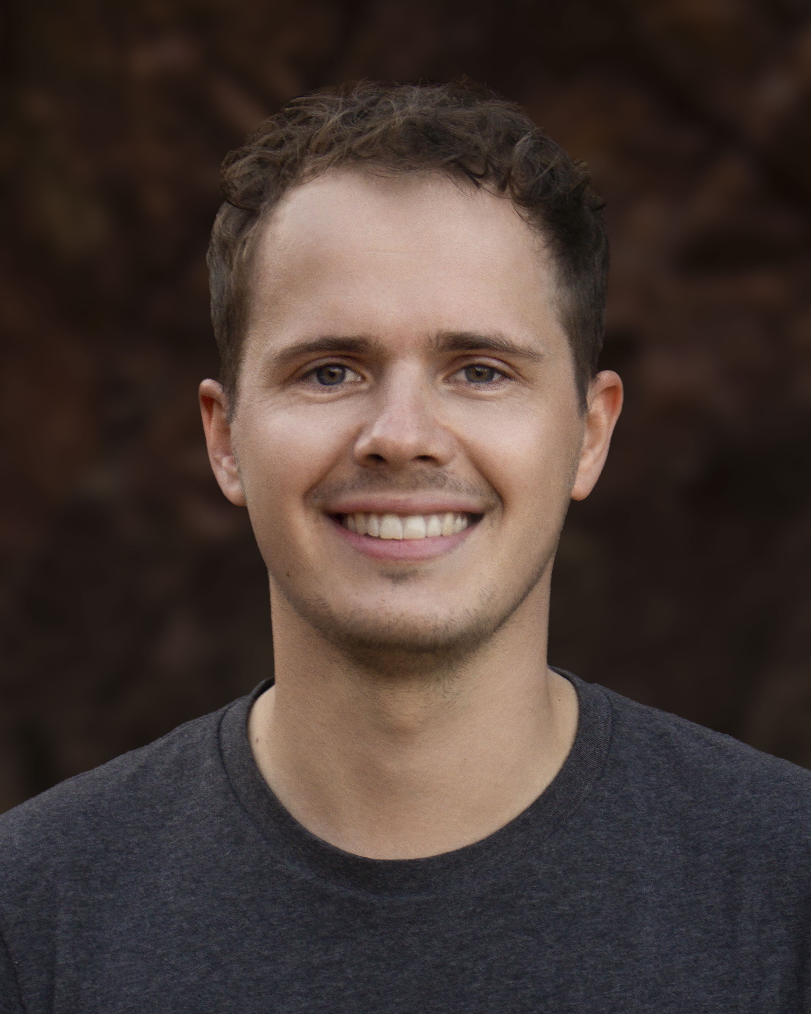 Portrait of Arthur Schiller smiling against a softly blurred brown background