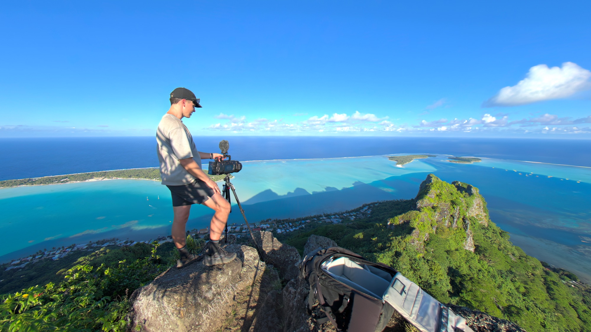 James Hustler filming with a tripod-mounted camera on the summit of Mount Teurafaatiu above the lagoon of Maupiti