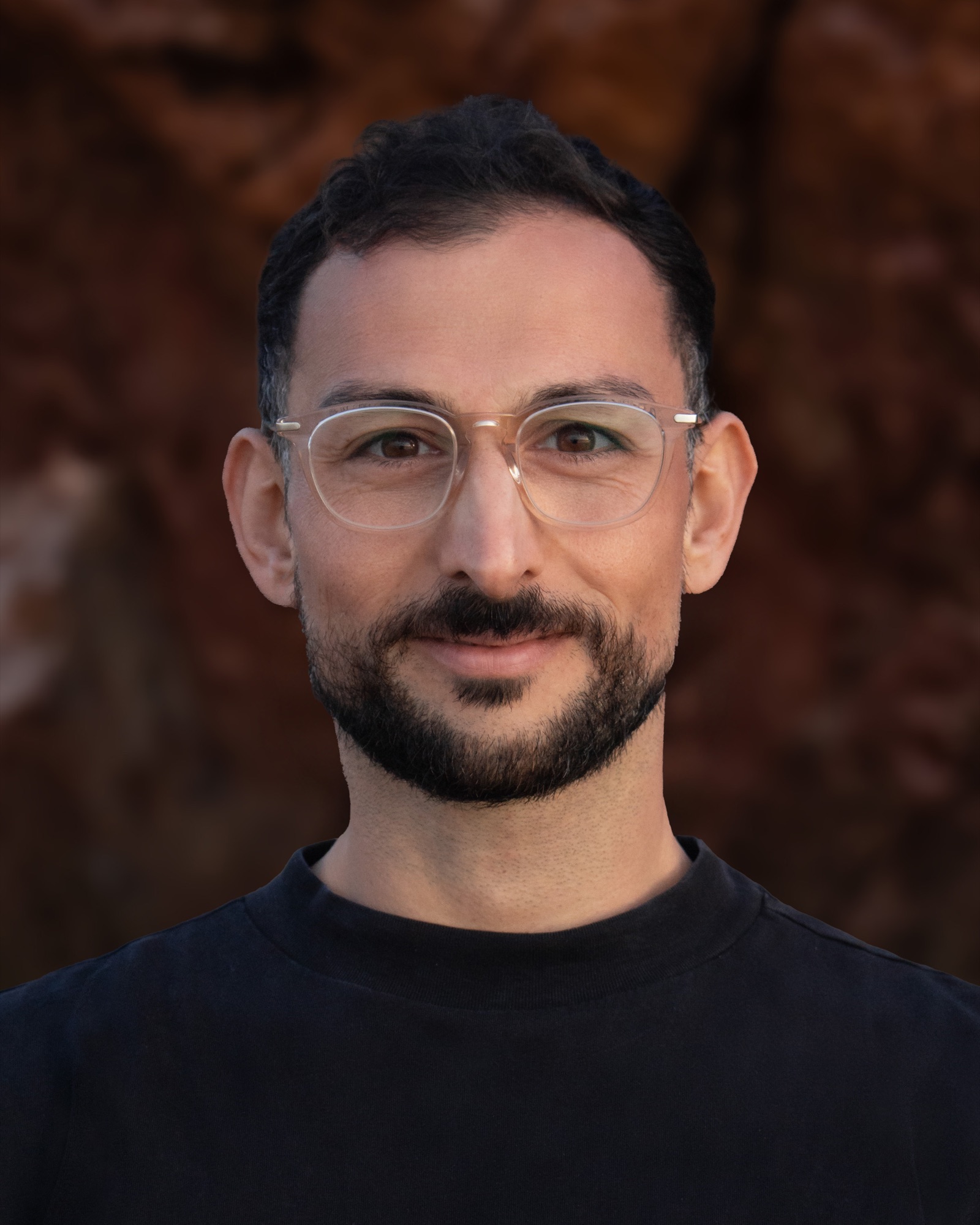 Portrait of Marc Wicht wearing clear-framed glasses against a softly blurred brown background