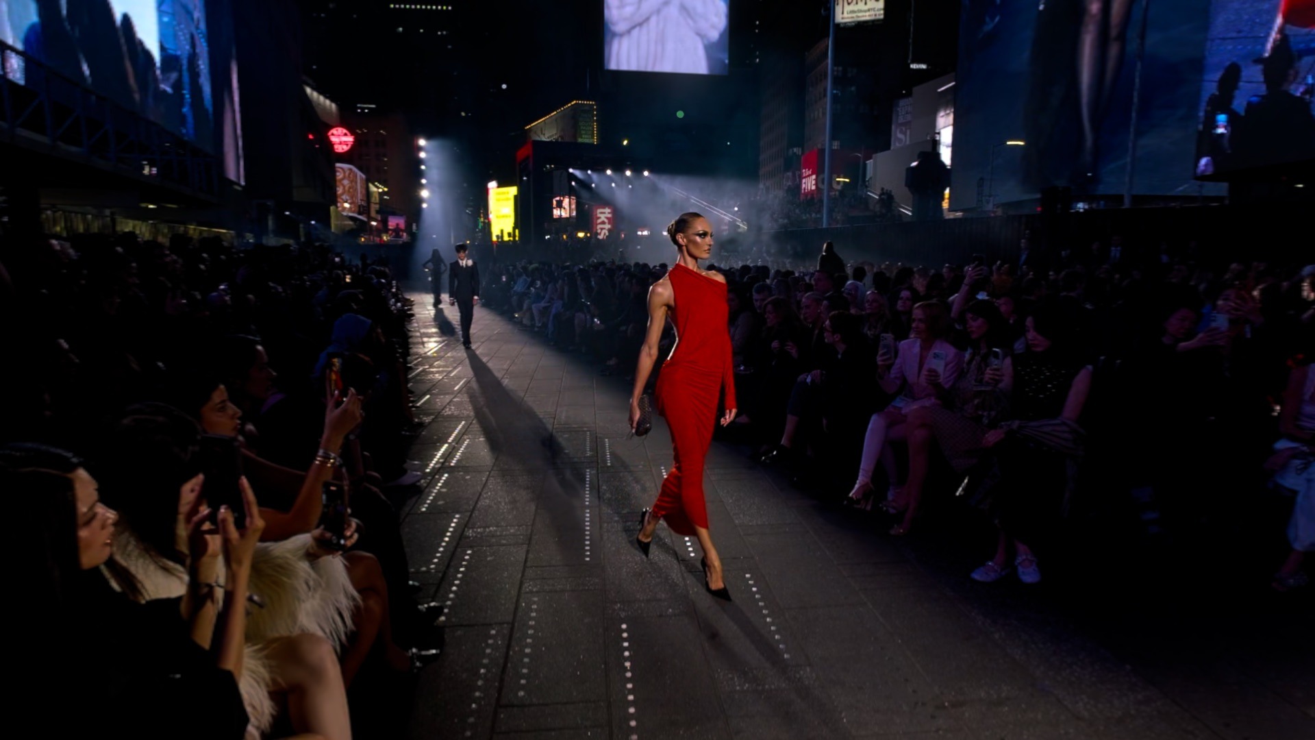 A model in a red dress walks between guests at Gucci’s GucciCore show in Times Square, shown in an official Gucci app screenshot
