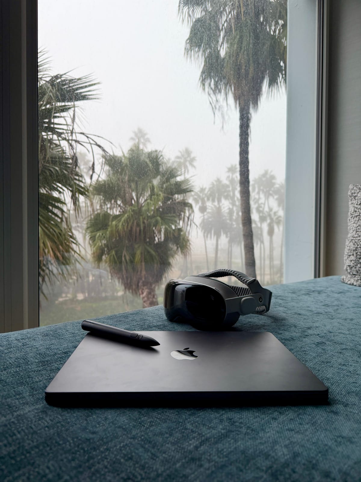 Apple Vision Pro and a MacBook arranged for work beside a rainy window