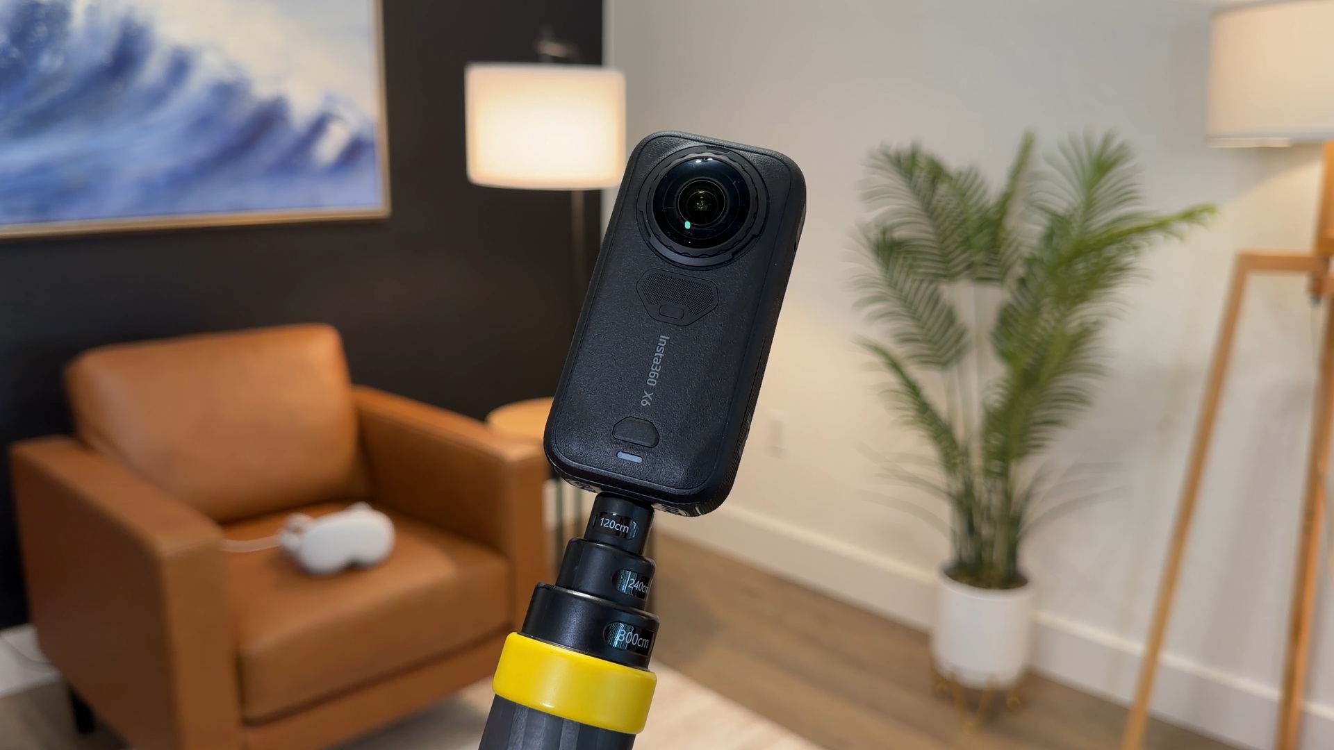 An Insta360 X6 camera on a selfie stick in our studio, with Apple Vision Pro on a chair behind it