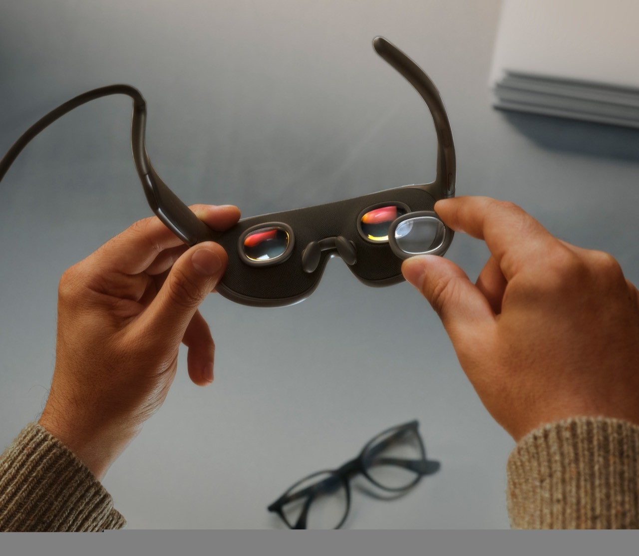Hands hold Meta VR Glasses with a separate lens insert beside one of the eyepieces.