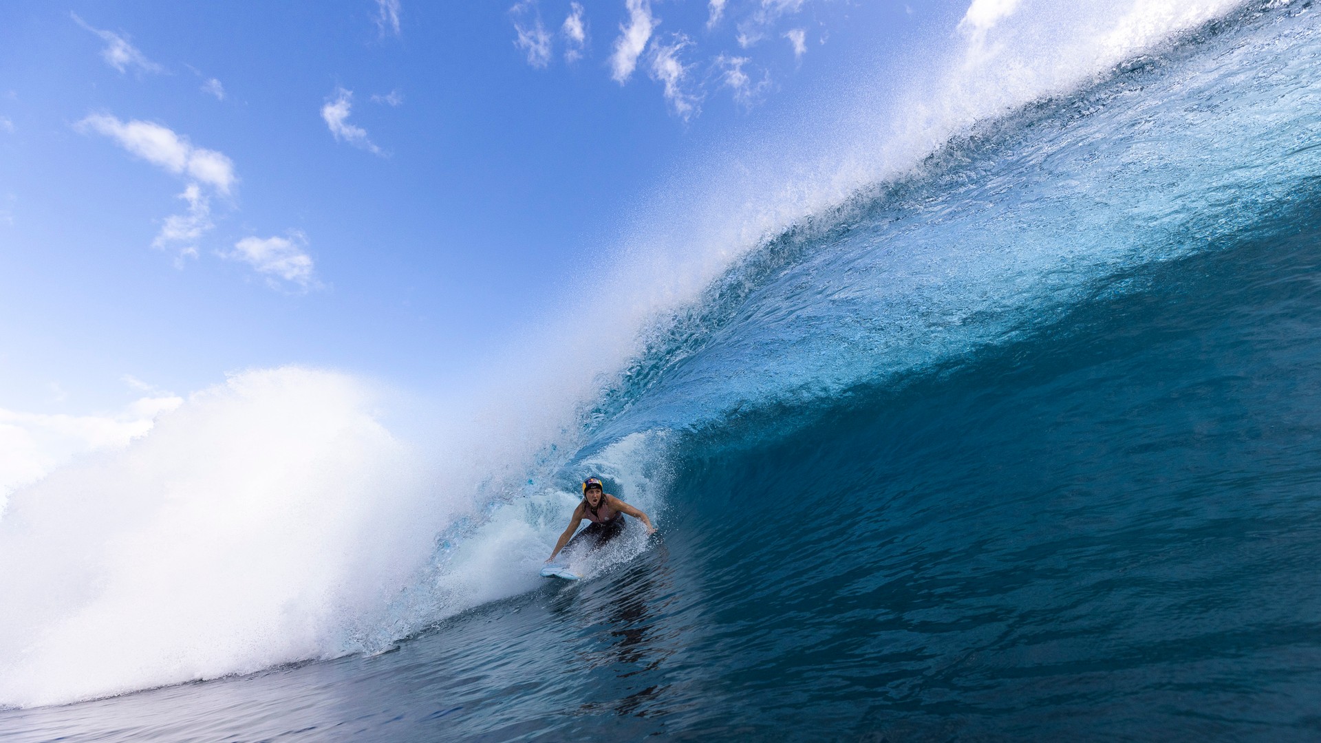 A surfer rides beneath a large curling blue wave at Teahupoʻo, Tahiti.
