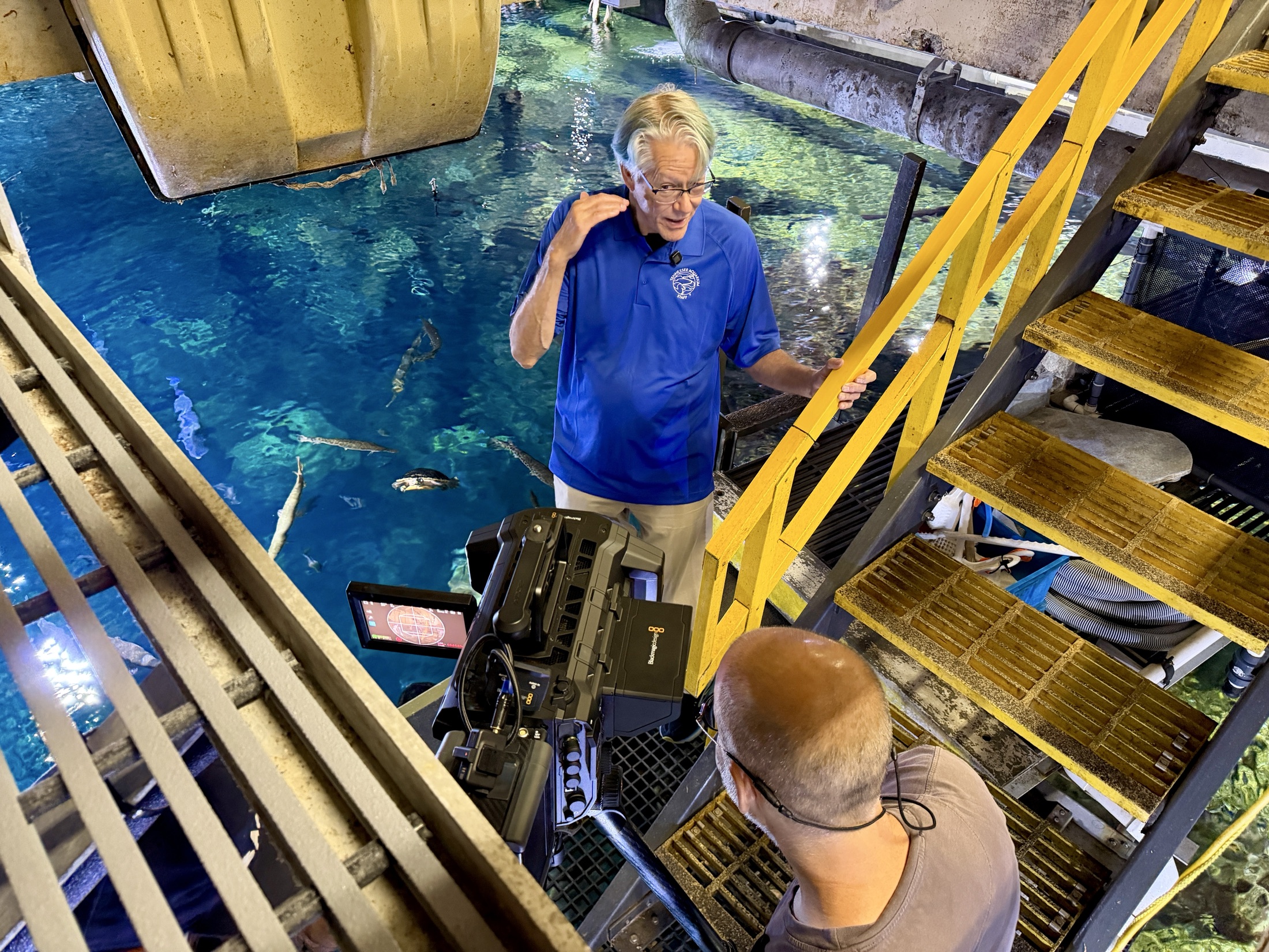 Jose Marquez stands beside an immersive camera above a large tank at the Tennessee Aquarium